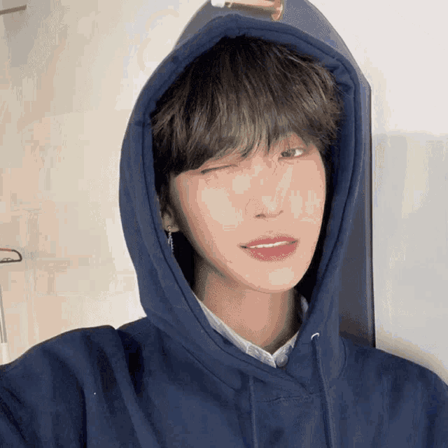 a young man wearing a blue hoodie is winking at the camera