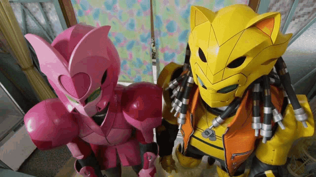 a pink robot and a yellow robot with dreadlocks stand next to each other