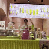a man in an apron stands behind a counter in front of a sign that says ' juice '