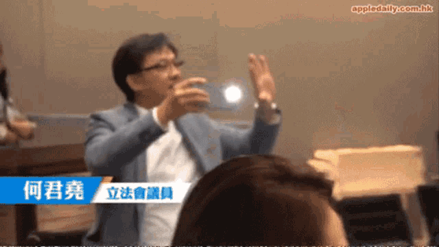 a man in a suit talks to a group of people with appledaily.com.hk at the bottom