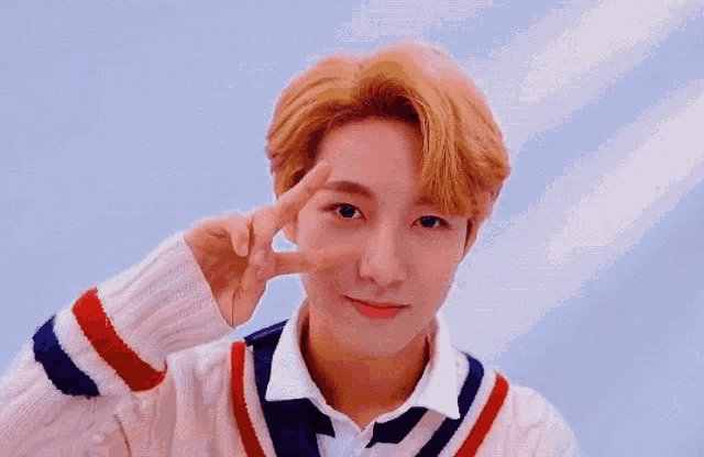 a young man in a sweater is making a peace sign with his hand .
