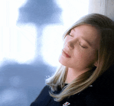 a woman leaning against a wall with her eyes closed and a badge on her shirt that says ' tommy hilfiger '