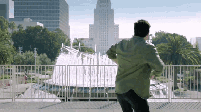 a man stands in front of a fountain in a city park