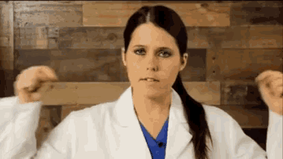 a woman in a lab coat and blue scrub is making a face
