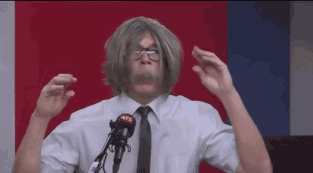 a man in a wig and tie is speaking into a microphone