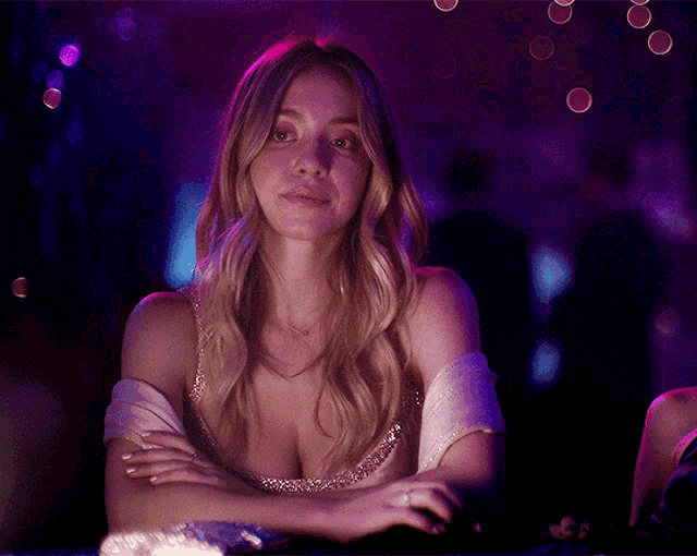 a woman sitting at a table with her arms crossed and a purple background