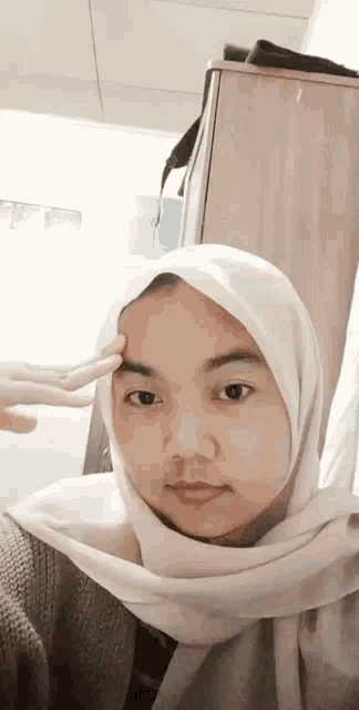 a woman wearing a white hijab is making a peace sign with her hands .