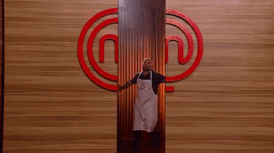 a man in an apron is standing in front of a wooden wall .