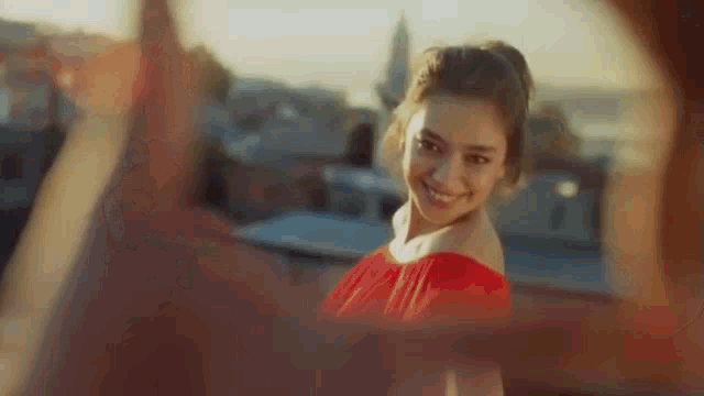 a woman in a red dress is smiling and looking at the camera while a man takes a picture of her .
