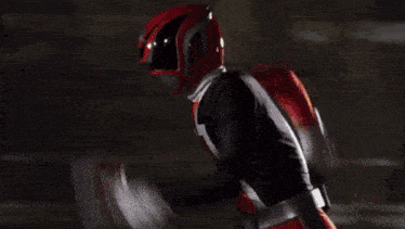a man in a red superhero costume is flying through the air in front of a large explosion .