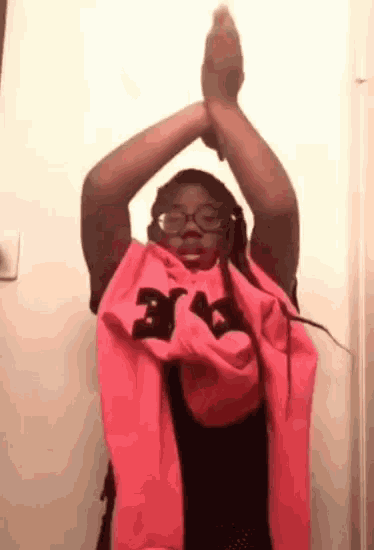 a woman wearing glasses and a pink scarf has her arms up in the air