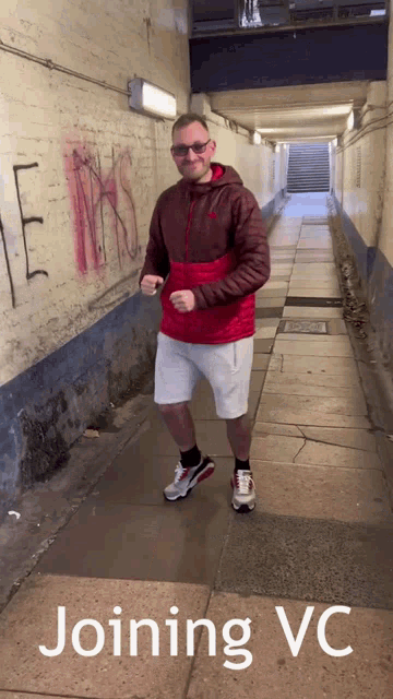 a man in a red jacket and white shorts is standing in a tunnel with the words joining vc written on the sidewalk