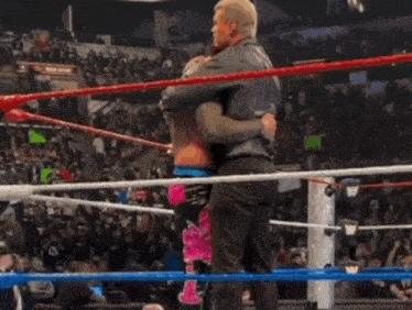 a wrestler is hugging another wrestler in a wrestling ring .