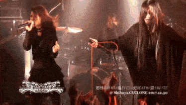 a woman singing into a microphone while a man plays drums