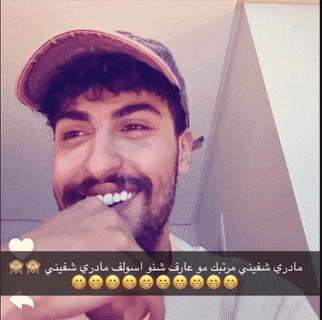 a man with a beard wearing a baseball cap is smiling with arabic writing below him