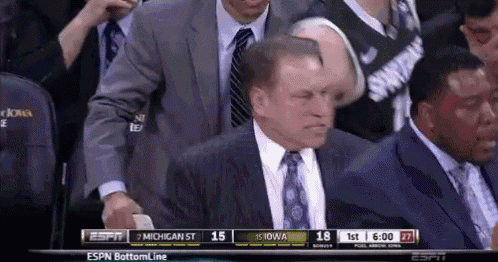 a man in a suit and tie watches a basketball game between michigan st and iowa state