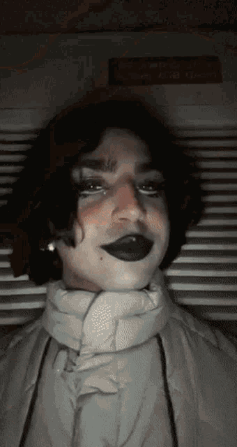 a person wearing black lipstick and a white jacket looks at the camera