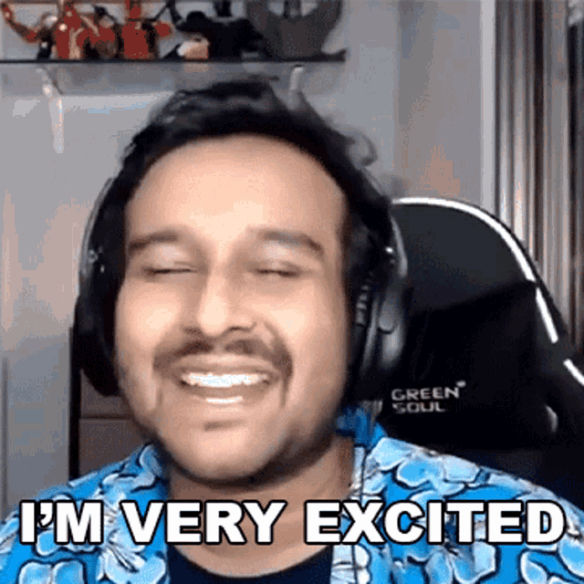 a man wearing headphones and a blue shirt is smiling and says `` i 'm very excited '' .