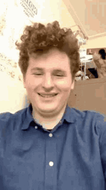 a man with curly hair is smiling and wearing a blue shirt