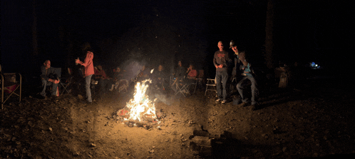 a group of people are gathered around a campfire in the woods