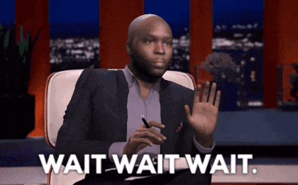 a man in a suit sits in a chair with the words wait wait wait below him