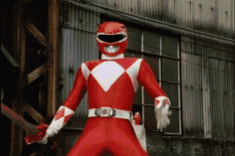 a red power ranger is standing in front of a building and holding a sword .