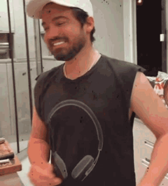 a man with a beard wearing a hat and headphones on his shirt is smiling .