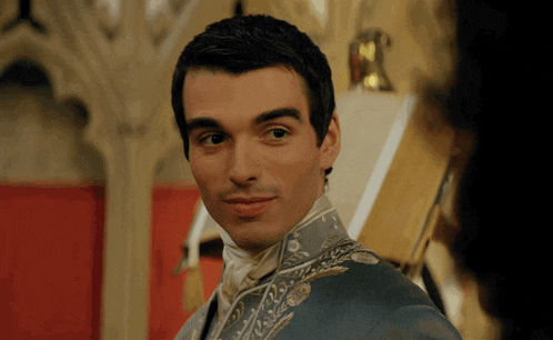 a man in a blue jacket with gold embroidery looks at a woman
