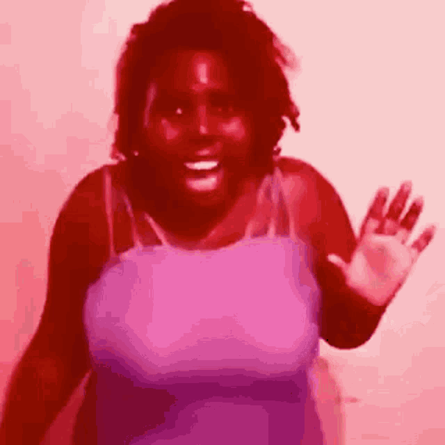 a woman in a purple tank top is smiling and waving her hand .