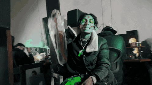 a man with green paint on his face is sitting in a chair with a necklace that says ' i love you ' on it