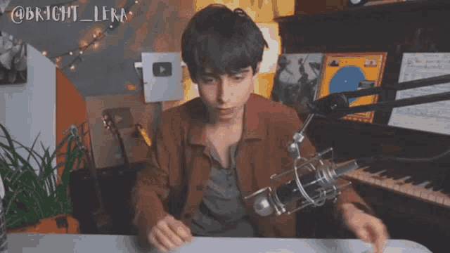 a young man is sitting at a desk in front of a microphone and a piano ..