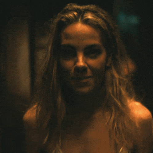 a woman in a white tank top is smiling in the dark