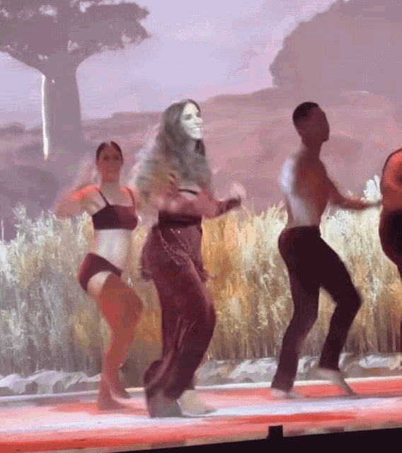 a group of people are dancing on a stage in front of a large screen