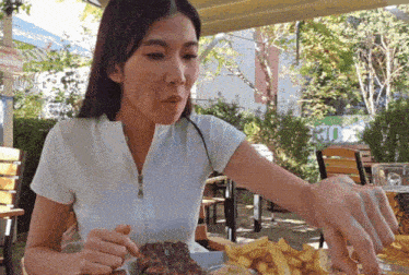 a woman in a white shirt is eating french fries and a large piece of meat