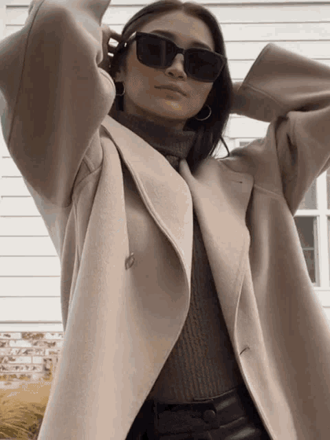 a woman wearing sunglasses and a coat is standing in front of a building