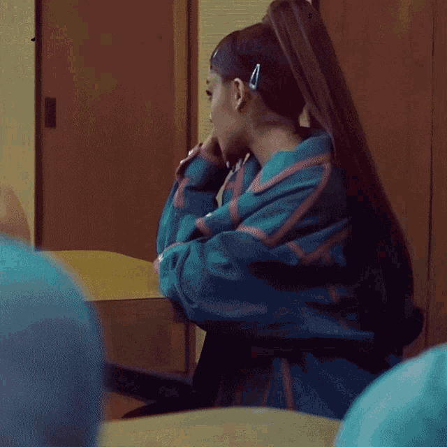 a woman in a blue and red jacket sits at a desk