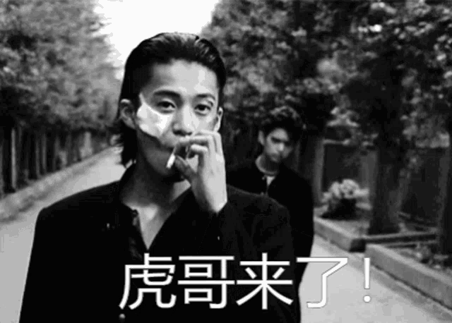 a man is smoking a cigarette in a black and white photo while another man looks on .