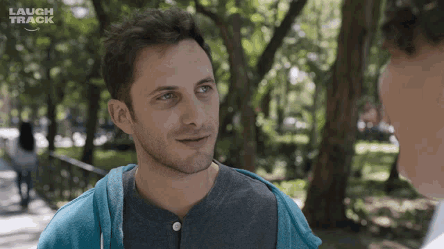 a man in a blue sweatshirt talks to another man in a park with the words laugh track on the bottom right
