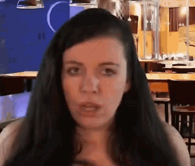 a woman with long black hair is standing in front of a kitchen with tables and chairs