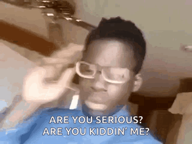 a young boy wearing glasses is talking on a cell phone and saying `` are you serious ? are you kidding me ? ''