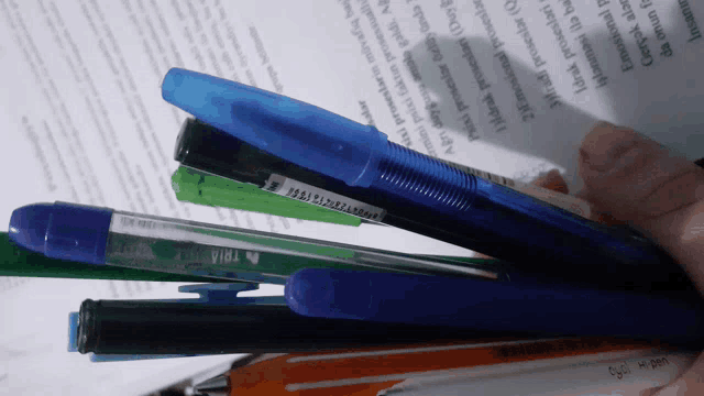 a person is holding a bunch of pens and a stapler on top of a paper