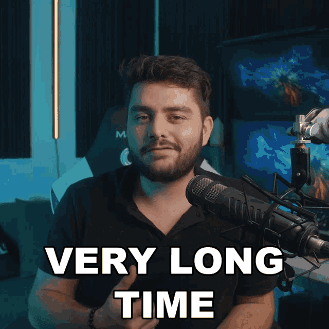 a man sitting in front of a microphone with the words very long time above him