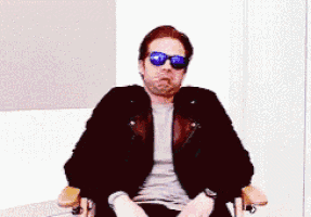 a man wearing sunglasses and a leather jacket is sitting in a chair .