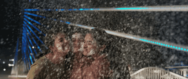 a couple kissing in front of a bridge with blue lights
