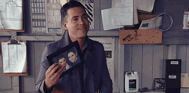 a man holds a framed picture of two men in front of a bulletin board that says ' secure ' on it