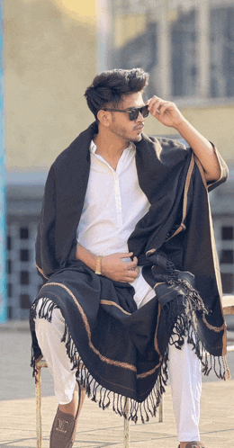 a man wearing a white shirt and a black shawl sits on a chair