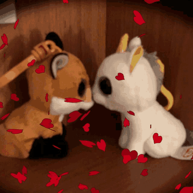 a stuffed animal fox and a stuffed animal unicorn kissing surrounded by red hearts