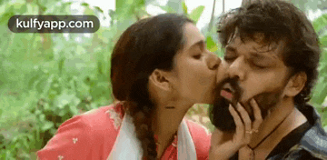 a woman is kissing a man on the cheek in the forest .