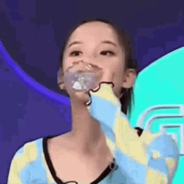 a woman is drinking water from a bottle while wearing a blue and yellow sweater .