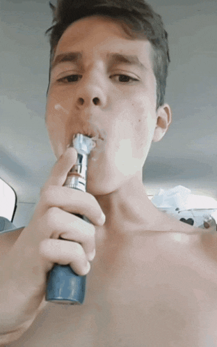 a shirtless man is smoking an electronic cigarette in a car